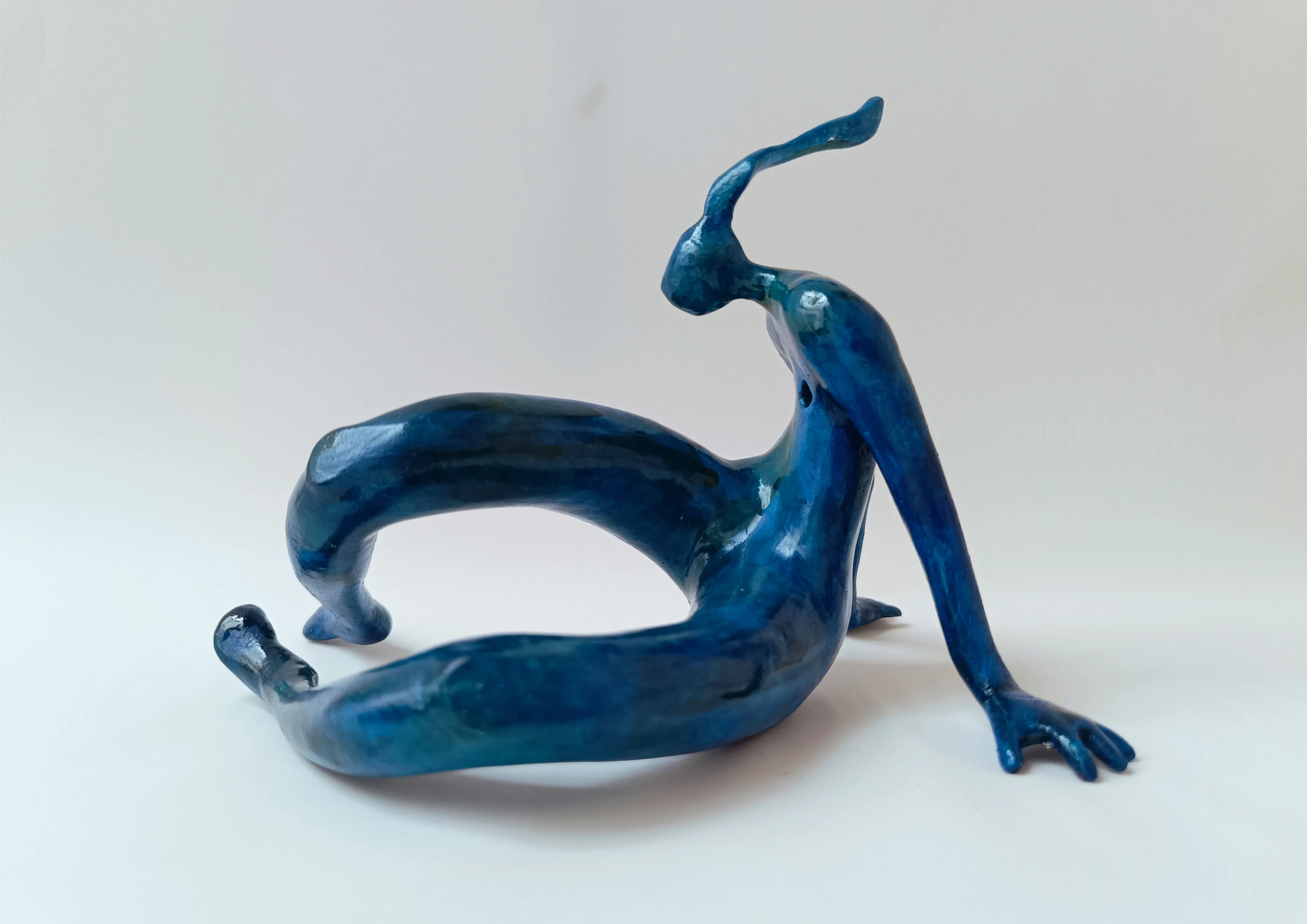 Figura sentada con las manos apoyadas en el suelo. Tonos azules. 13x13x17 centímetros, 253 gramos